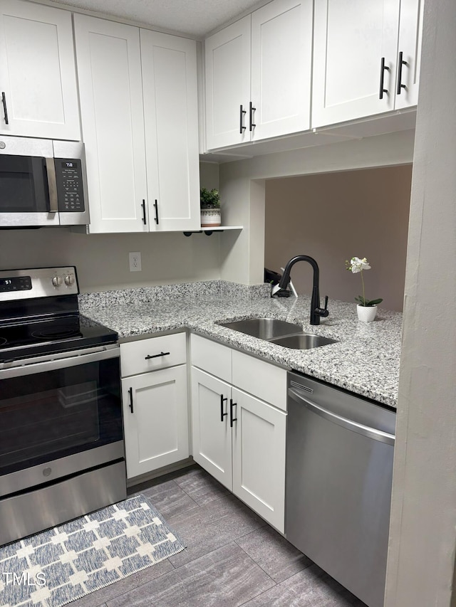 kitchen featuring a sink, light stone counters, wood finished floors, appliances with stainless steel finishes, and white cabinets