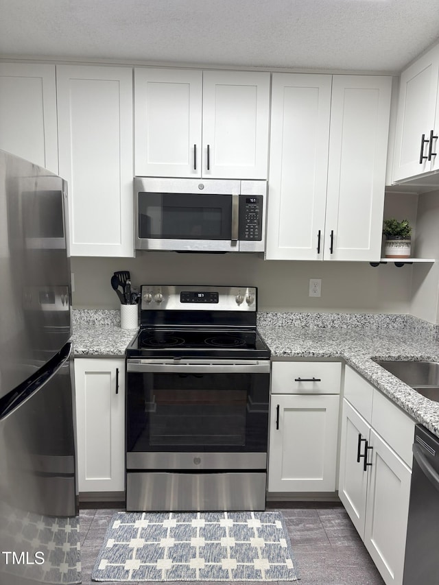 kitchen featuring light stone countertops, stainless steel appliances, a textured ceiling, white cabinetry, and open shelves