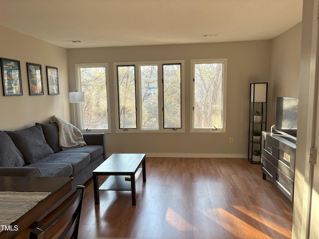 living room featuring baseboards, plenty of natural light, visible vents, and wood finished floors