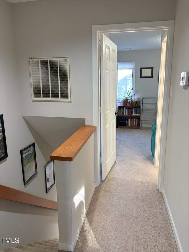 hallway featuring visible vents, light colored carpet, and baseboards