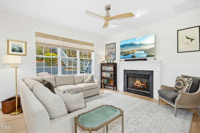 living room featuring wood finished floors, visible vents, and a warm lit fireplace