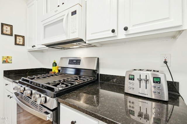 kitchen featuring dark stone countertops, wood finished floors, white microwave, stainless steel gas range oven, and white cabinetry