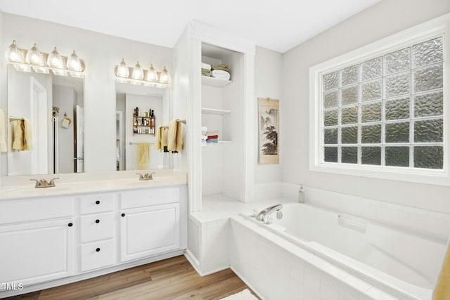 bathroom with a sink, a garden tub, wood finished floors, and double vanity