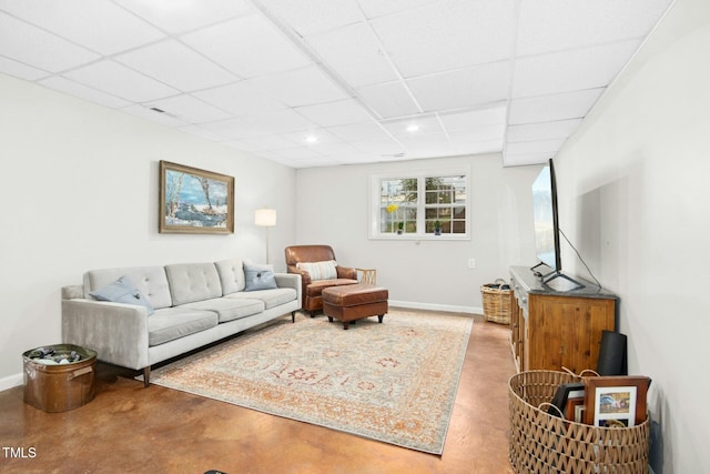 living area featuring a paneled ceiling, baseboards, and concrete flooring