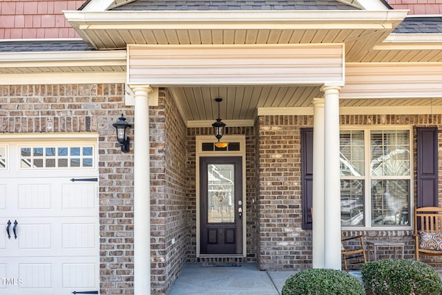 view of exterior entry featuring brick siding, covered porch, a shingled roof, and a garage