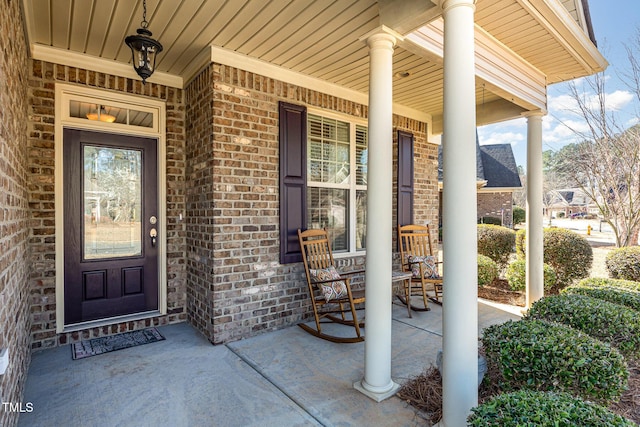 view of exterior entry with brick siding and a porch