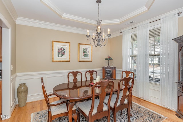 dining room with wainscoting, an inviting chandelier, a raised ceiling, and light wood-style floors