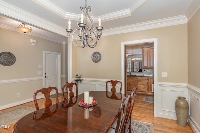 dining room with light wood-style flooring, a tray ceiling, an inviting chandelier, wainscoting, and a decorative wall