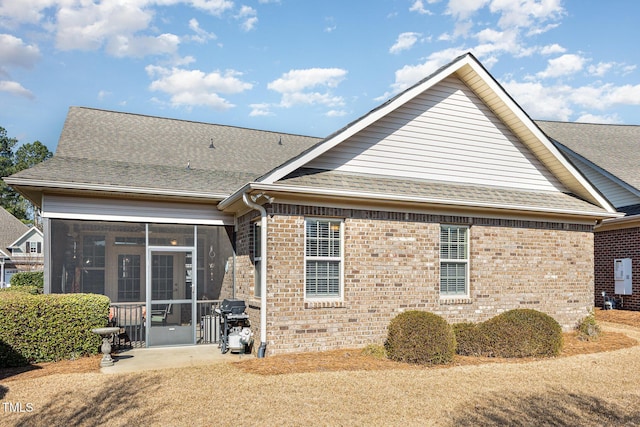 back of house with brick siding, a sunroom, and roof with shingles