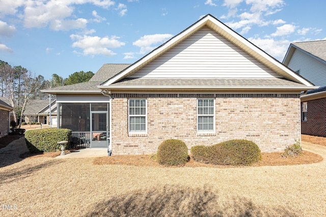 rear view of property featuring brick siding, roof with shingles, and a sunroom