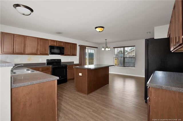 kitchen featuring a kitchen island, dark wood finished floors, a chandelier, black appliances, and a sink