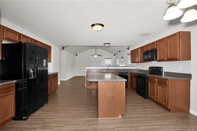 kitchen featuring brown cabinets, black appliances, wood finished floors, a peninsula, and lofted ceiling