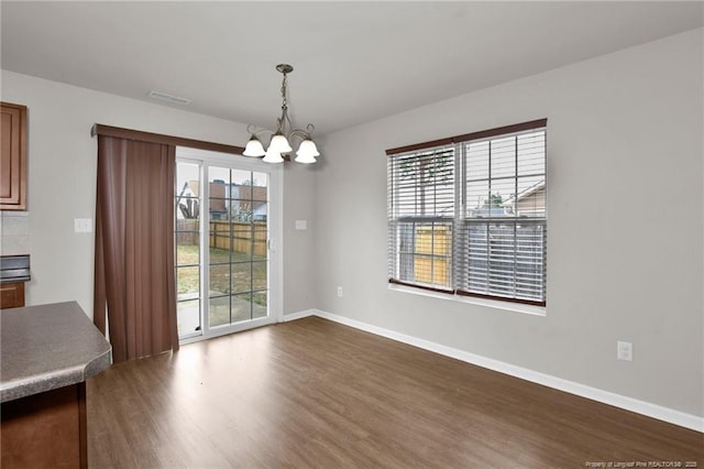 unfurnished dining area featuring dark wood finished floors, a notable chandelier, visible vents, and baseboards