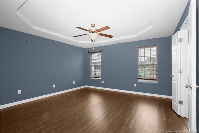 unfurnished room featuring baseboards, a raised ceiling, a healthy amount of sunlight, and dark wood finished floors