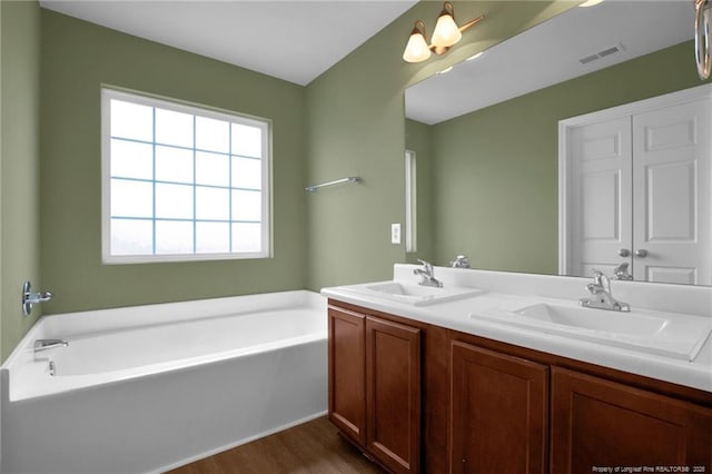 full bathroom featuring wood finished floors, visible vents, double vanity, a sink, and a garden tub