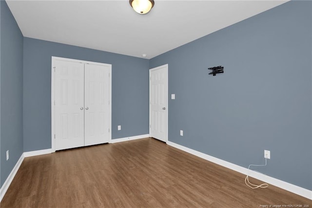 unfurnished bedroom with wood finished floors, baseboards, and a closet