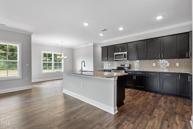 kitchen featuring a center island with sink, a sink, stainless steel appliances, dark wood-type flooring, and tasteful backsplash