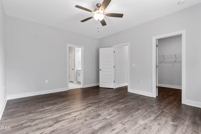 unfurnished bedroom with a spacious closet, wood finished floors, a closet, and baseboards