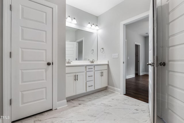 bathroom featuring double vanity, baseboards, marble finish floor, and a sink