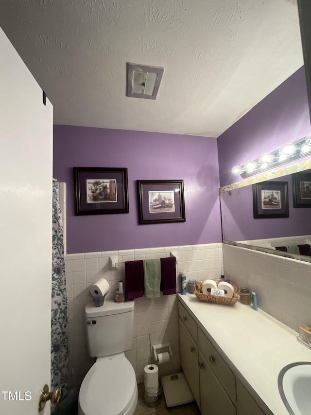 bathroom featuring a wainscoted wall, a textured ceiling, vanity, and toilet