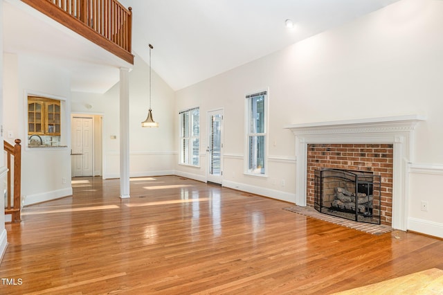 unfurnished living room featuring light wood-style flooring, a fireplace, high vaulted ceiling, and baseboards