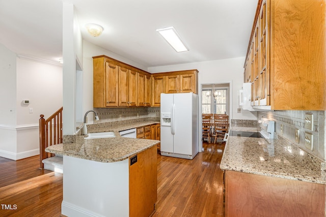 kitchen with white appliances, light stone counters, a peninsula, a sink, and brown cabinets