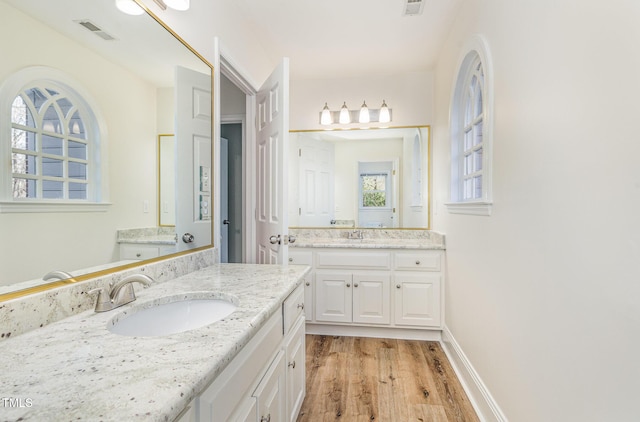 full bath featuring visible vents, baseboards, two vanities, wood finished floors, and a sink