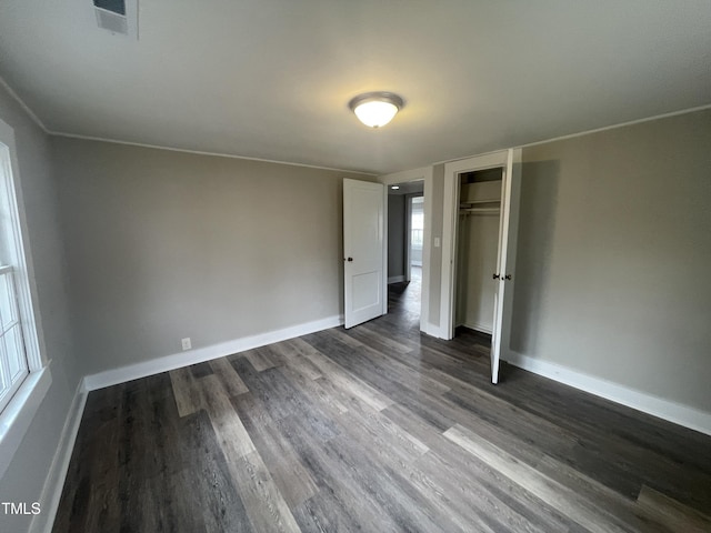 unfurnished bedroom with a closet, baseboards, dark wood-type flooring, and visible vents