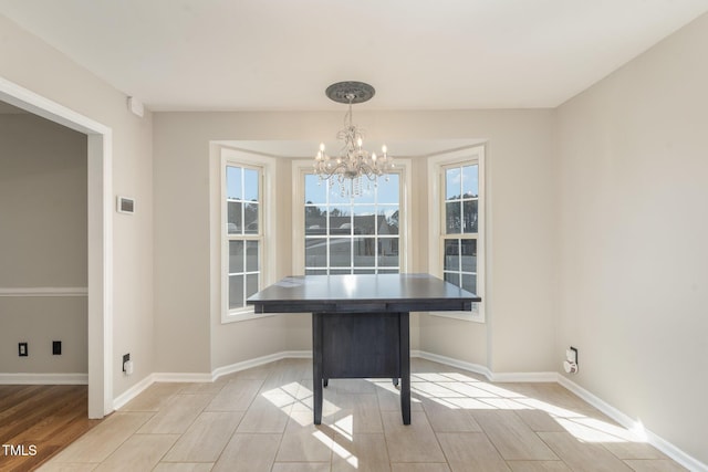 unfurnished dining area with light wood finished floors, an inviting chandelier, and baseboards