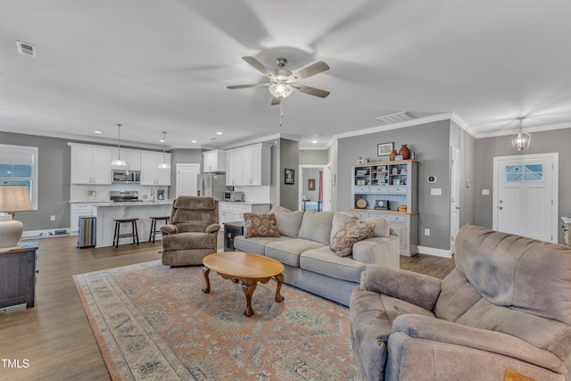 living room featuring visible vents, ceiling fan, crown molding, and light wood-style flooring