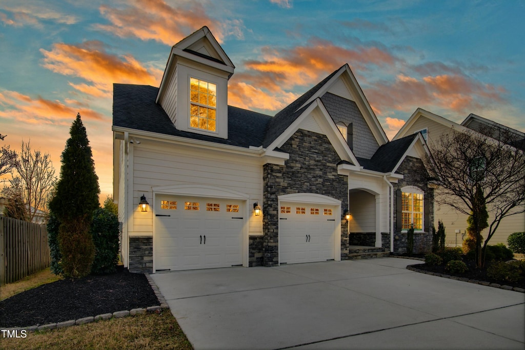 view of front facade featuring a shingled roof, driveway, fence, and stone siding