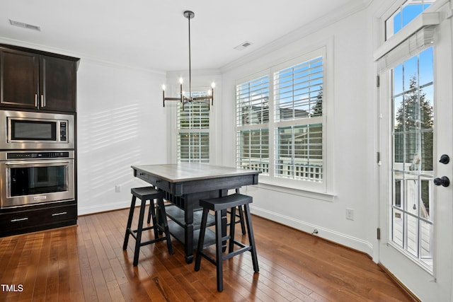 dining area with dark wood finished floors, visible vents, an inviting chandelier, and ornamental molding