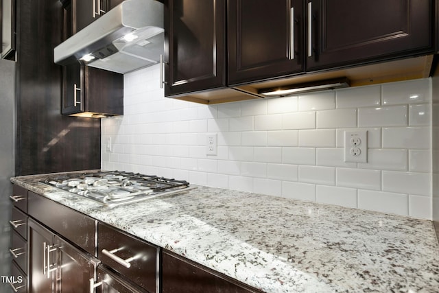 kitchen with under cabinet range hood, dark brown cabinetry, decorative backsplash, light stone countertops, and stainless steel gas cooktop