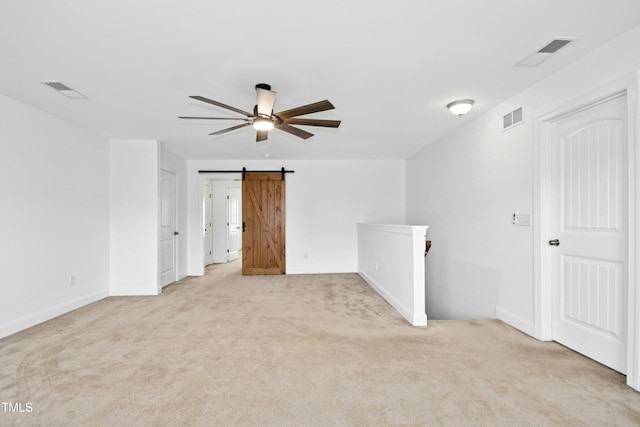 spare room with visible vents, a barn door, and light colored carpet