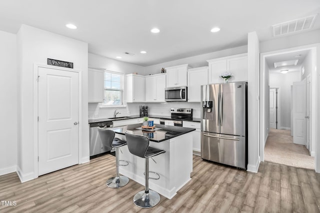 kitchen featuring visible vents, a kitchen island, a sink, white cabinets, and appliances with stainless steel finishes