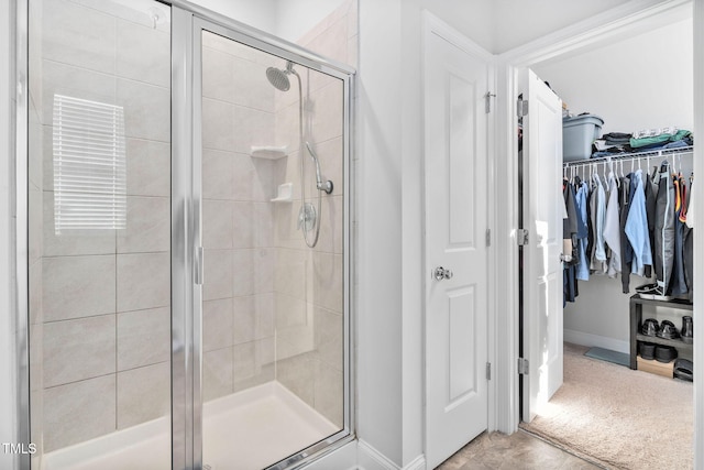 bathroom with a walk in closet, baseboards, and a stall shower