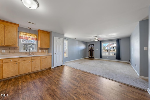 kitchen with a ceiling fan, a sink, light countertops, dark wood-type flooring, and backsplash