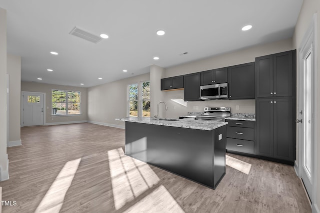 kitchen with light wood finished floors, visible vents, light stone counters, appliances with stainless steel finishes, and a sink