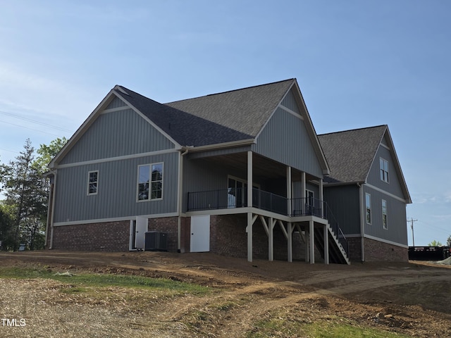 exterior space featuring stairway, cooling unit, a shingled roof, and brick siding