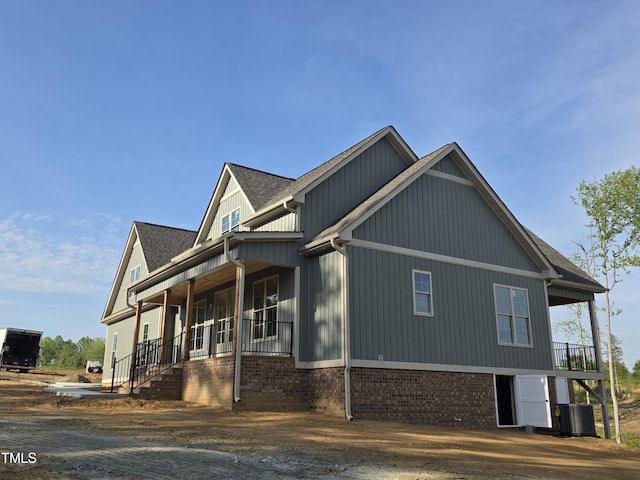 view of property exterior featuring covered porch, brick siding, central AC, and roof with shingles