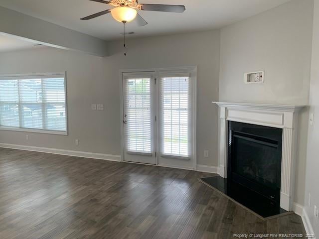 unfurnished living room featuring dark wood finished floors, a glass covered fireplace, a healthy amount of sunlight, and baseboards