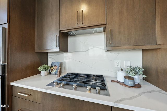 kitchen with under cabinet range hood, light stone countertops, backsplash, and stainless steel gas cooktop