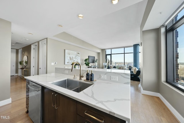 kitchen featuring light wood-style flooring, a sink, open floor plan, dark brown cabinets, and dishwasher