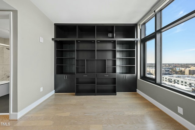 unfurnished bedroom featuring a view of city, light wood-style flooring, and baseboards