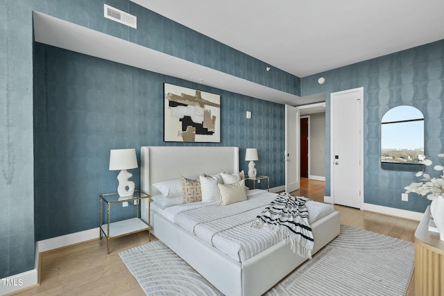 bedroom featuring visible vents, baseboards, wood finished floors, and an accent wall