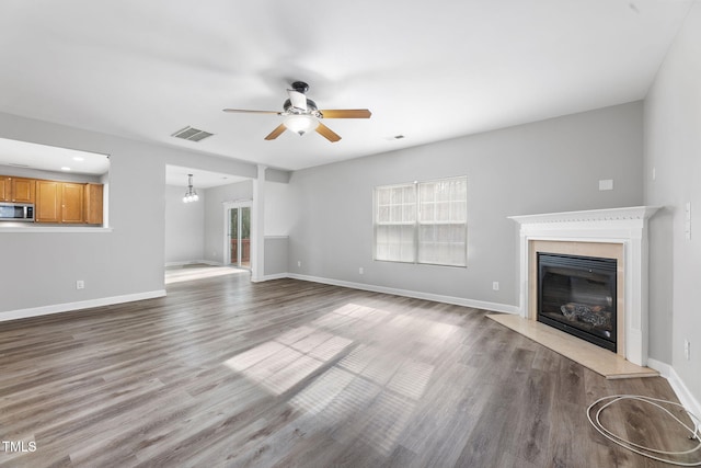 unfurnished living room with visible vents, ceiling fan with notable chandelier, wood finished floors, a premium fireplace, and a healthy amount of sunlight