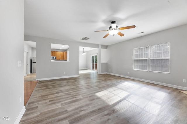 unfurnished living room featuring ceiling fan with notable chandelier, visible vents, light wood finished floors, and baseboards