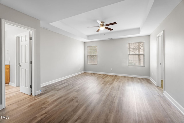 spare room featuring baseboards, a ceiling fan, light wood-type flooring, and a tray ceiling