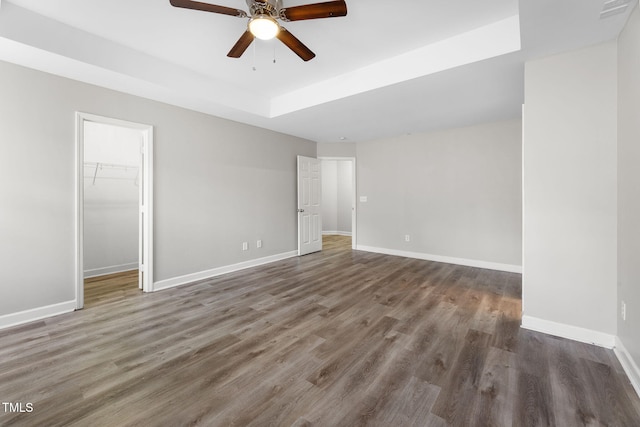 unfurnished bedroom featuring a raised ceiling, a ceiling fan, wood finished floors, baseboards, and a spacious closet