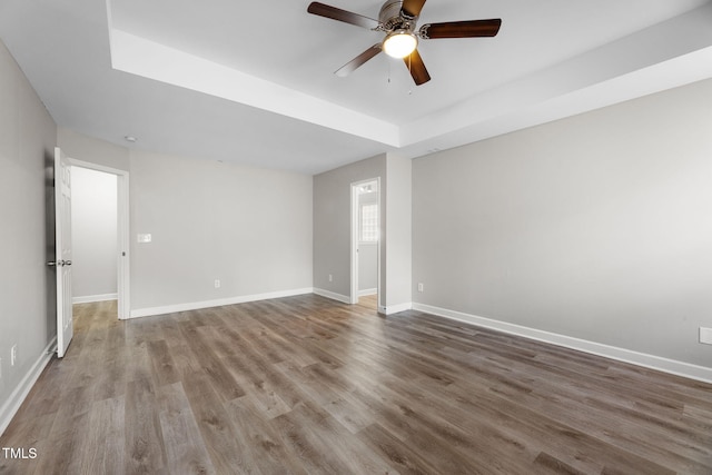 spare room featuring a tray ceiling, baseboards, wood finished floors, and a ceiling fan